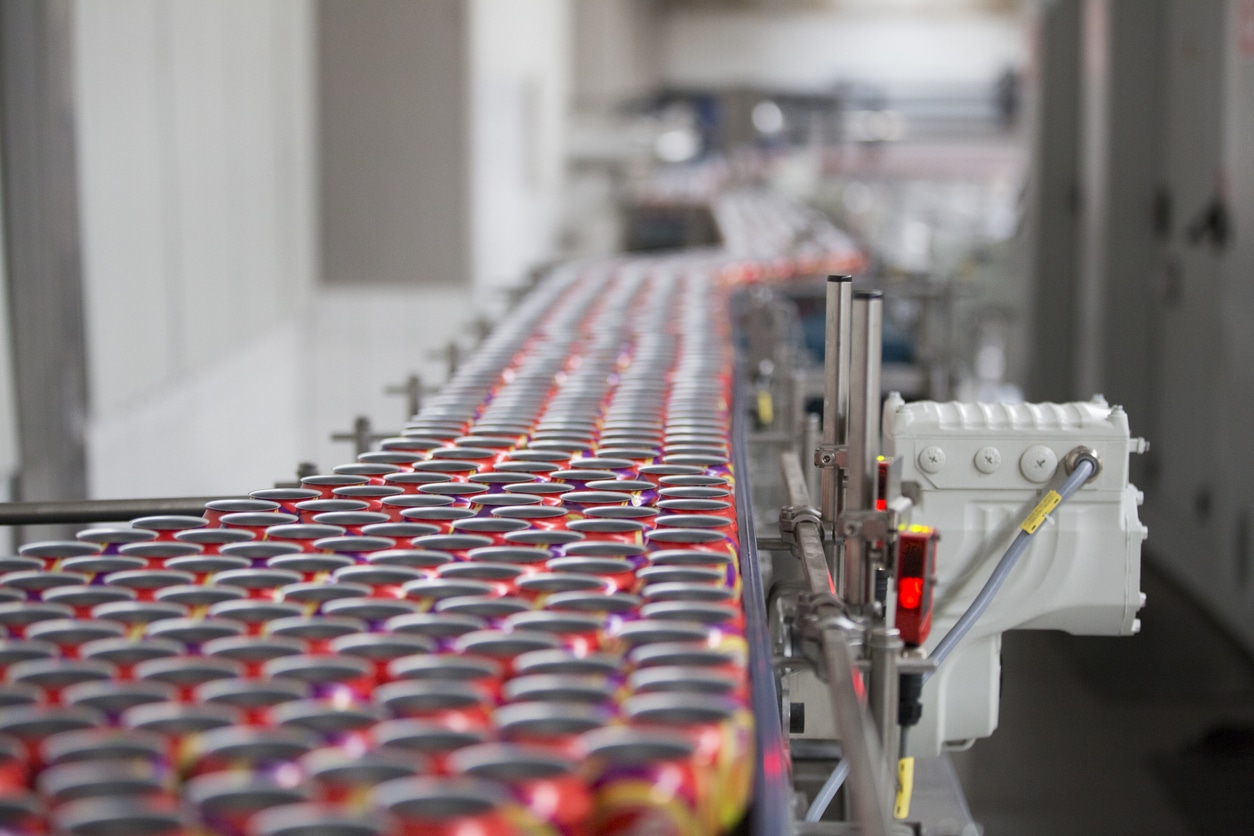 A long conveyor belt transports rows of aluminum cans through a factory production line, efficiently moving these essential consumer packaged goods.