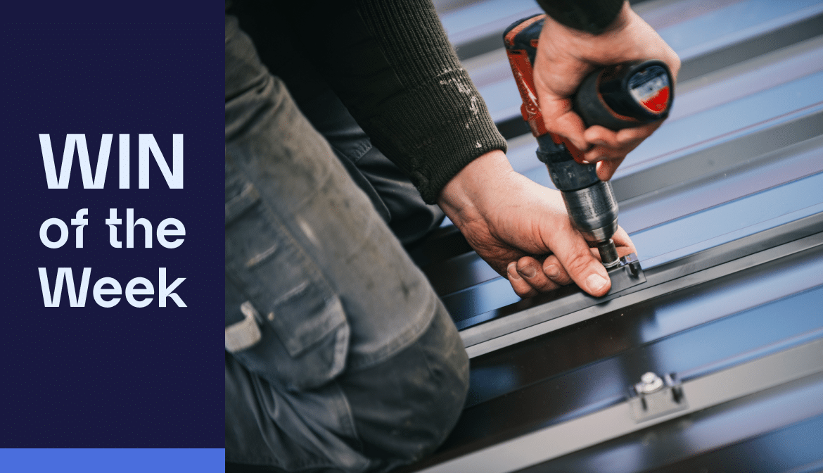 Close-up of a person using a power drill to secure a metal panel. Text on the left reads "Save .2M WIN of the Week" in bold white letters on a dark blue background.